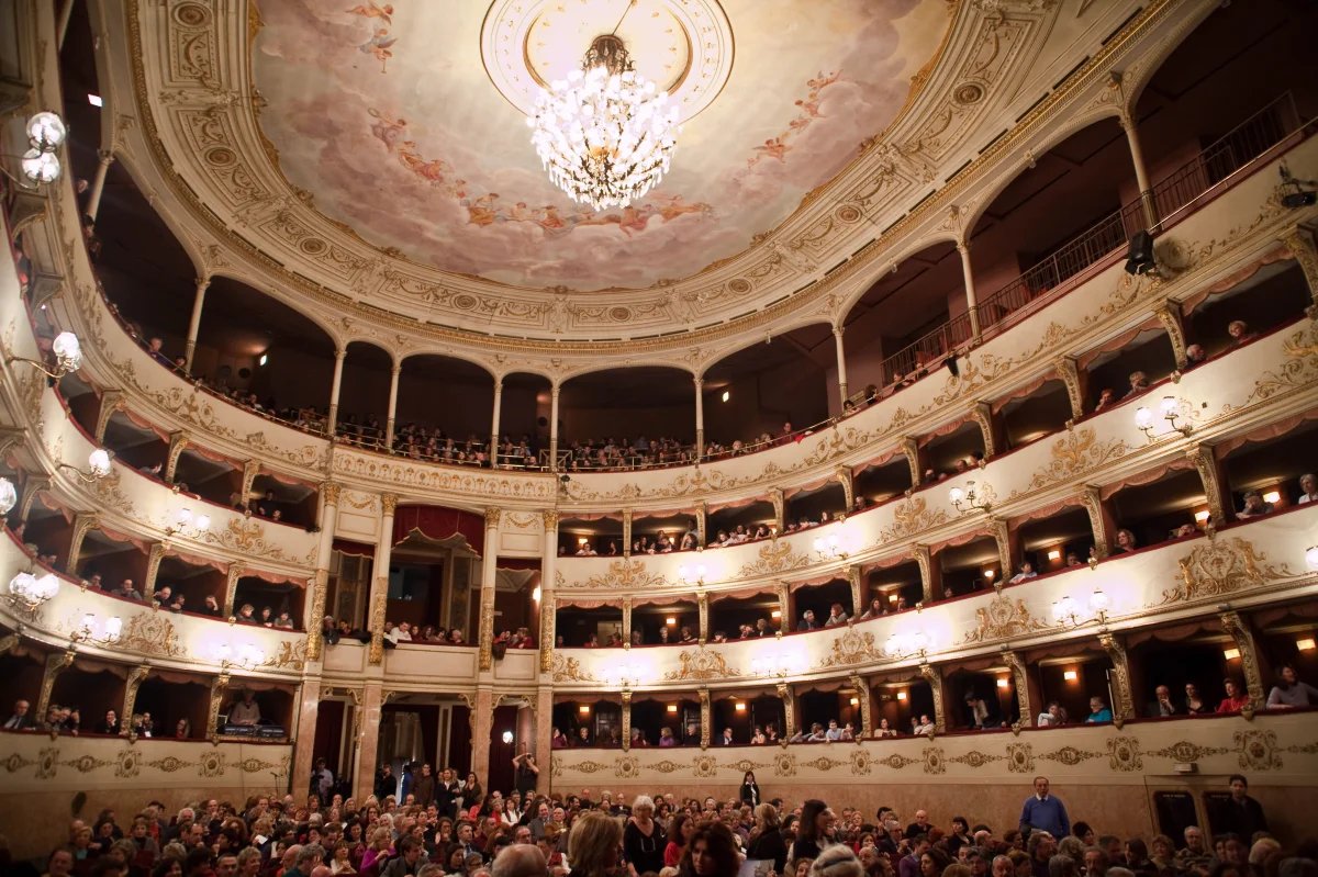 Una splendida vista dello storico Teatro della Pergola, che mostra la sua grandiosa architettura e il suo intricato design. Il teatro presenta una facciata splendidamente decorata, caratterizzata da dettagli ornamentali ed elementi classici che riflettono il suo ricco patrimonio culturale. In primo piano, l'ingresso dell'Atrio delle Colonne è incorniciato da eleganti colonne e motivi decorativi, che invitano il pubblico a entrare. L'illuminazione calda esalta l'atmosfera invitante, mentre l'area circostante è probabilmente animata da attività, suggerendo il ruolo vibrante del teatro nella comunità. La composizione complessiva evidenzia la bellezza e il significato del Teatro della Pergola, rendendolo un punto focale di eventi culturali e spettacoli, utile anche per eventi aziendali.